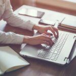 Person sitting at a desk typing on a laptop.