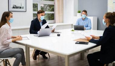 Employees with masks sitting around a desk.