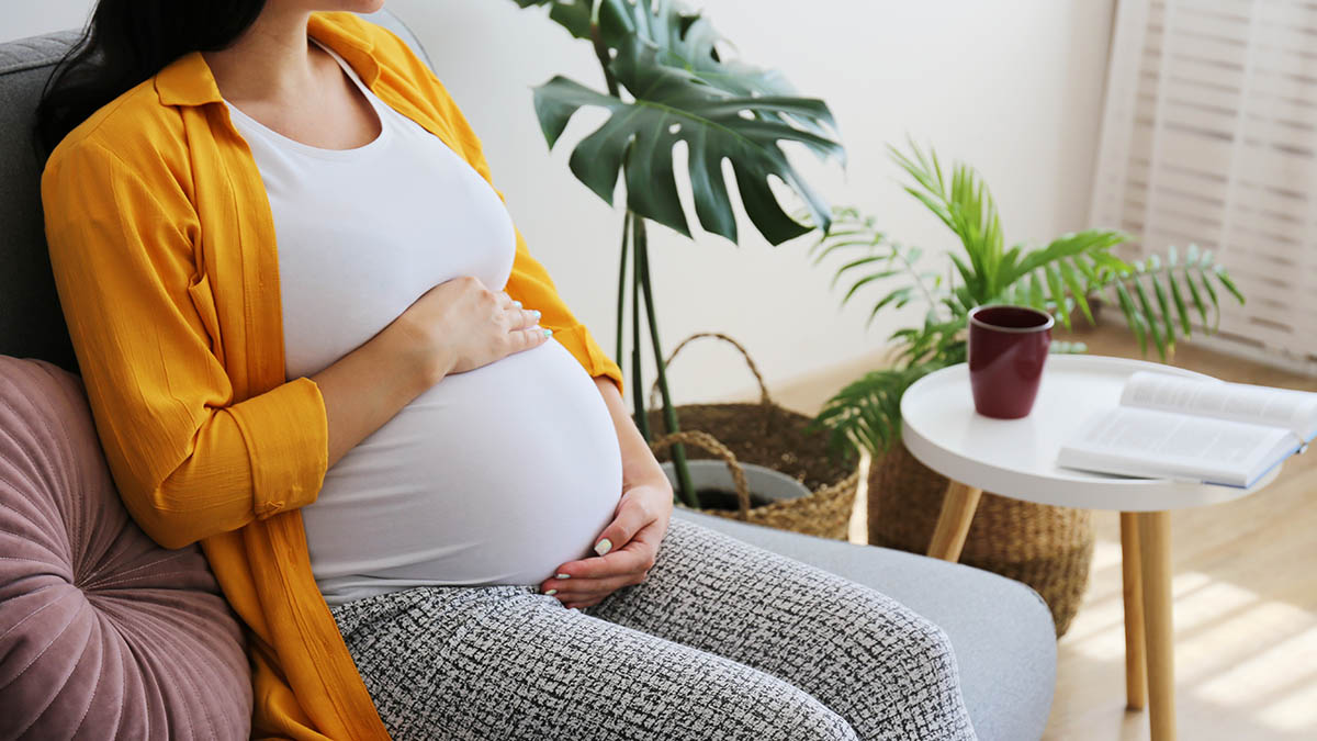 Cropped shot of young beautiful woman on third trimester of pregnancy. Close up of pregnant female with arms on her round belly.