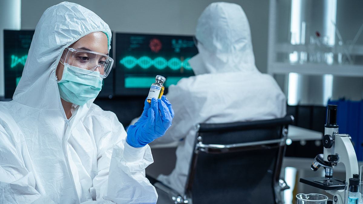 Researcher, wearing a mask, holds an mRNA vaccine vial