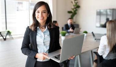 Smiling female holding a laptop in a conference room with a team in the background