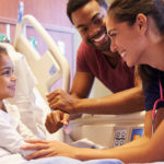 Pediatric doctor visiting young girl in hospital dad with dad smiling in the background