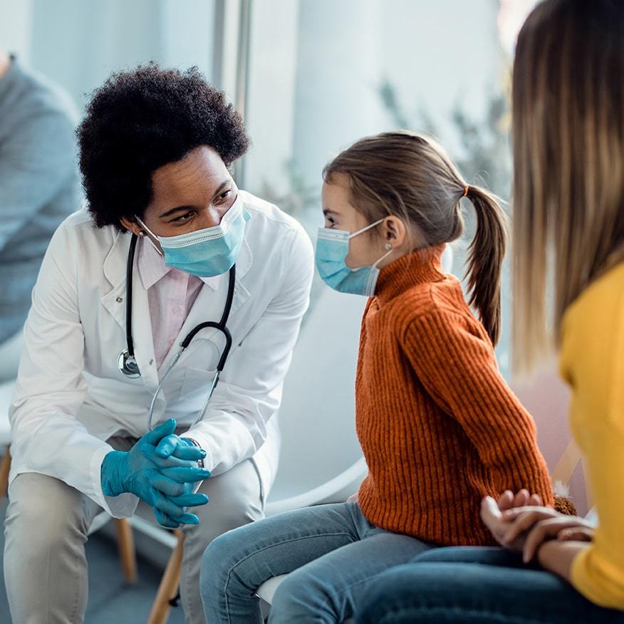 Doctor speaking with child and her mother in a clinical setting.
