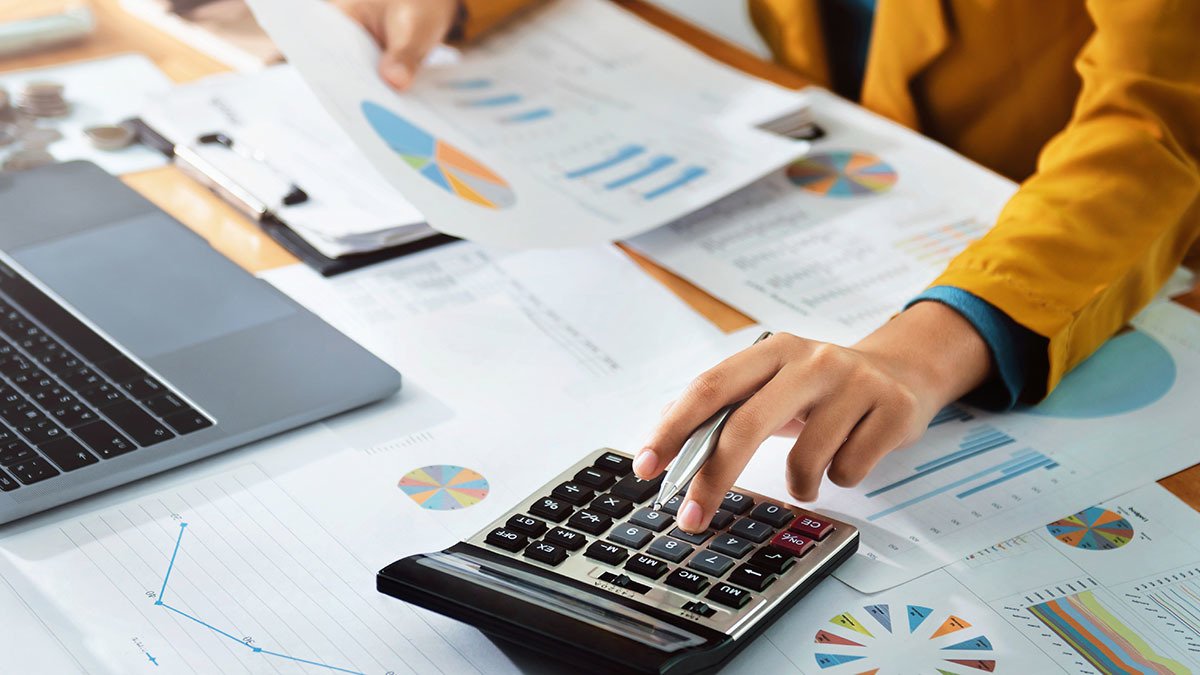 Female using calculator and computer, while holding pen and analyzing graphs and charts