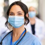 Close-up shot of masked female nurse, with other nurses and doctors masked standing in the background behind her