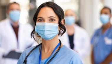 Close-up shot of masked female nurse, with other nurses and doctors masked standing in the background behind her