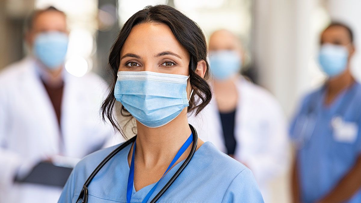Close-up shot of masked female nurse, with other nurses and doctors masked standing in the background behind her
