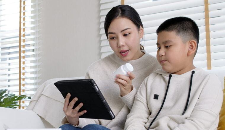 Mother holding a prescription bottle having a video chat with a doctor.