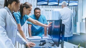A diverse team of medical scientists solve problems and point at computer screens showing various scans.