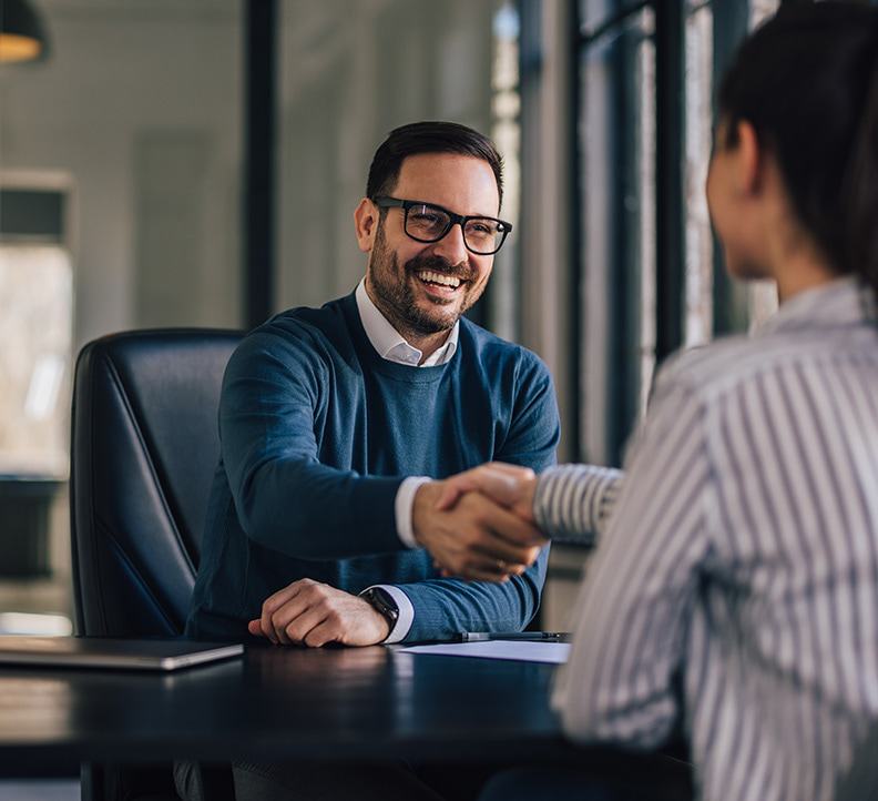 Two business partners shaking hands while seated at a table.