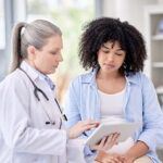 Doctor speaking to a patient while holding a tablet.