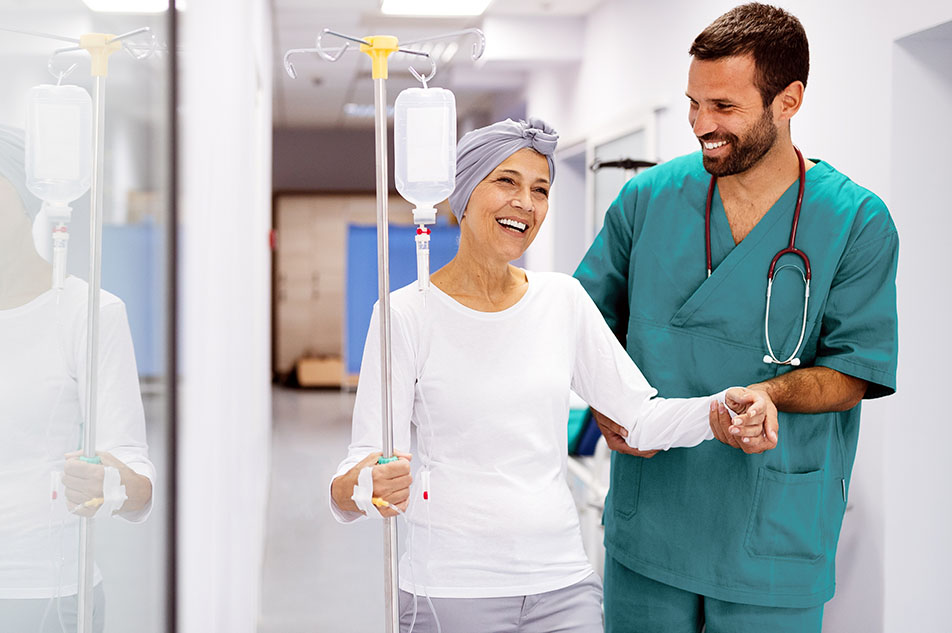 An early phase oncology clinical trial participant walking down the hallway with the assistance of a nurse.