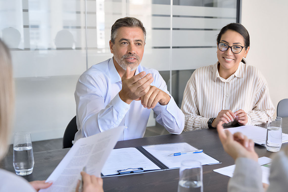 Professionals having a conversation during a meeting while seated at a conference table.