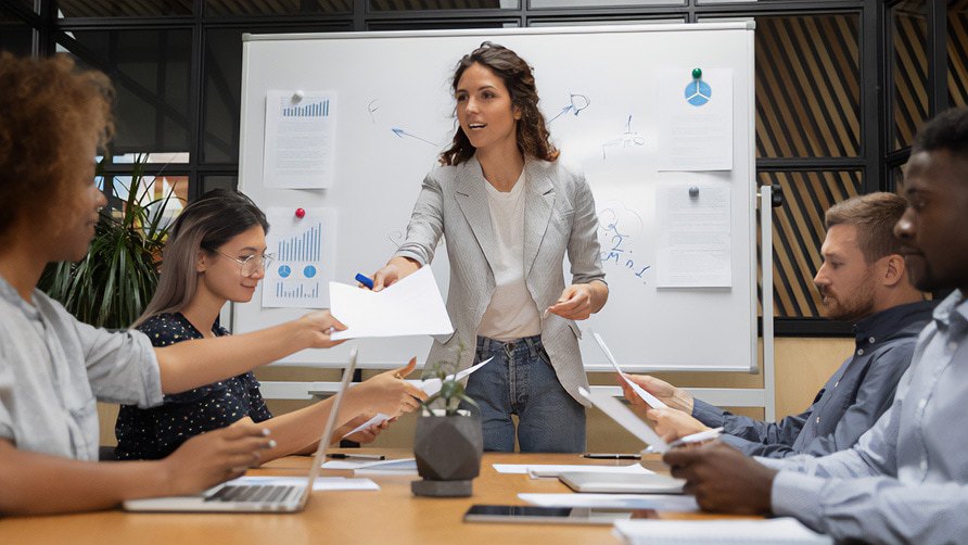Five business professionals having a meeting with a white board in the back.
